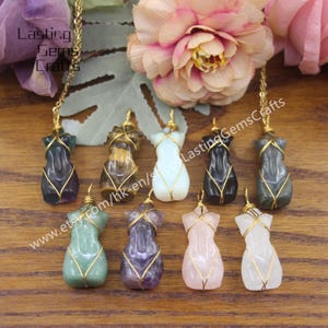 May include: Eight different colored gemstone pendants in the shape of a female torso, each wrapped in gold wire. The pendants are arranged in a row on a wooden surface. The text "www.etsy.com/hk-en/shop/LastingGemsCrafts" is visible in the image.