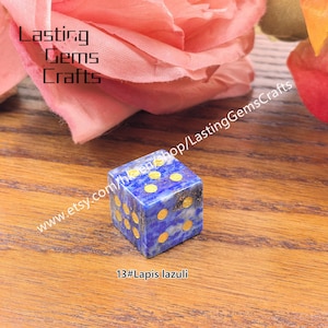 May include: A blue lapis lazuli dice with gold-colored dots. The dice is cube-shaped and sits on a wooden surface. The text "Lasting Gems Crafts" is visible in the background, along with the text "www.etsy.com/shop/LastingGemsCrafts" and "13#Lapis lazuli".