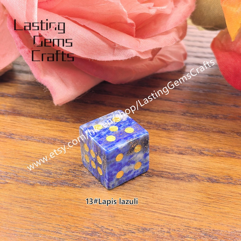 May include: A blue lapis lazuli dice with gold-colored dots. The dice is cube-shaped and sits on a wooden surface. The text "Lasting Gems Crafts" is visible in the background, along with the text "www.etsy.com/shop/LastingGemsCrafts" and "13#Lapis lazuli".