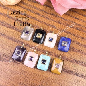 May include: A collection of rectangular gemstone pendants in various colors, including black, white, blue, and pink, each with a square gemstone inset. The pendants are displayed on a wooden surface, with the text "Lasting Gems Crafts" visible.