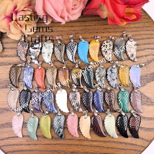 May include: A collection of gemstone wing pendants in various colors and patterns, displayed on a wooden surface. The pendants feature intricate carved details and silver-toned bails. The text "Lasting Gems Crafts" is visible in the upper left corner.
