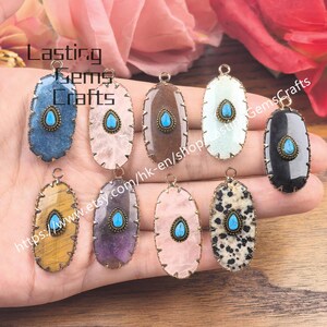 Op de afbeelding: Een verzameling ovaalvormige edelsteenhangers met een turquoise druppelvormige steen in het midden. De hangers hebben een goudkleurig metalen frame en hebben verschillende steenkleuren en patronen. De tekst "Lasting Gems Crafts" is zichtbaar.