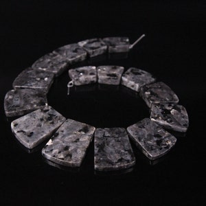 May include: A strand of black and grey gemstone beads, each bead is a rectangular shape with rounded edges. The beads are arranged in a spiral pattern.