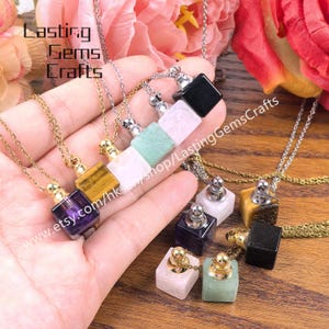 May include: A collection of gemstone pendant necklaces in various colors, including purple, yellow, green, pink, and black. Each necklace features a small, square gemstone bottle with a silver or gold-colored cap. The text "Lasting Gems Crafts" is visible.