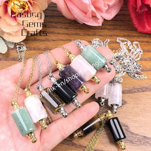Puede incluir: Una colección de collares con colgantes de piedras preciosas en varios colores, incluyendo verde, rosa, negro y ojo de tigre. Cada colgante tiene forma cilíndrica con detalles metálicos dorados y cuelga de una delicada cadena. El texto "Lasting Gems Crafts" es visible.