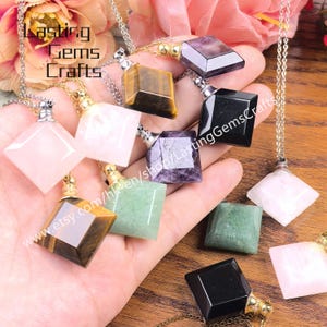 May include: A collection of gemstone pendant necklaces in various colors, including pink, green, black, and tiger's eye. Each pendant is a geometric shape with a metal cap and chain. The image includes the text "Lasting Gems Crafts" and a website address.