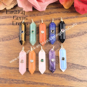 May include: Ten double-terminated hexagonal gemstone pendants arranged in two rows. Each pendant features a small circular metal-set stone accent. The stones include tiger's eye, green aventurine, orange, blue lapis lazuli, black, pink, and purple.