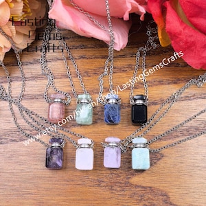 May include: A collection of gemstone vial necklaces in various colors, including pink, green, blue, and black. Each vial is suspended from a silver-colored chain. The image includes the text "Lasting Gems Crafts" and a website address.