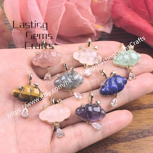 May include: A collection of gemstone cloud pendants in various colors, including pink, green, blue, and yellow. Each pendant features a gold-colored bail and a dangling teardrop-shaped charm. The text "Lasting Gems Crafts" is visible in the upper left corner.