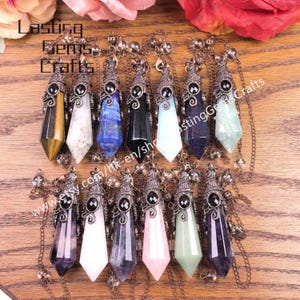 Peut inclure: Une collection de colliers pendentifs en pierres précieuses de différentes couleurs, dont le jaune, le blanc, le bleu, le noir et le rose. Chaque pendentif est une forme de cristal unique, suspendu à un capuchon et une chaîne en métal décoratifs. Le nom de la boutique Etsy "Lasting Gems Crafts" est visible.
