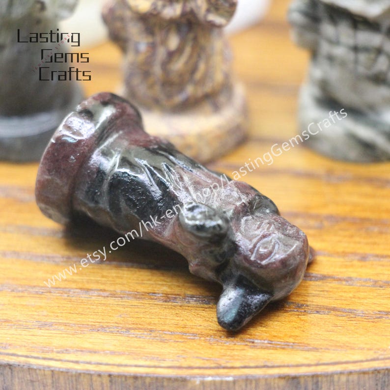 May include: A close-up of a black and red stone chess piece. The piece is shaped like a horse's head and is lying on its side. The piece is made of a smooth, polished stone. The piece is on a wooden surface. The text "www.etsy.com/hk-en/shop/LastingGemsCrafts" is visible in the image.