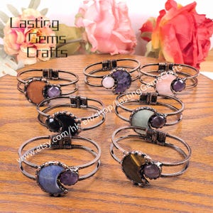 May include: A collection of handcrafted bracelets with various gemstone accents. Each bracelet features a double-banded, bronze-toned metal design. Gemstones include a variety of colors and shapes, such as round, crescent, and oval. The text "Lasting Gems Crafts" is visible.