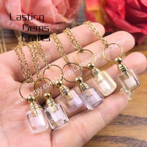 May include: A collection of gold-colored chain necklaces, each featuring a small, clear glass bottle pendant with a gold-colored cap. The bottles contain various colored crystals. The image includes the text "Lasting Gems Crafts" and a website address.