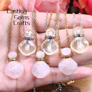Op de afbeelding: Verschillende edelsteen hangerkettingen met heldere en roze kristallen flesjes. De flesjes zijn bevestigd aan gouden en zilveren kettingen. De kettingen worden gepresenteerd tegen een zachtroze achtergrond. De tekst "Lasting Gems Crafts" en een websiteadres zijn zichtbaar.