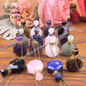 Pode incluir: Uma coleção de frascos de perfume de pedras preciosas em várias cores, incluindo roxo, rosa, azul e castanho. Cada frasco tem um design facetado único e é suspenso por uma corrente dourada. Os frascos são exibidos numa superfície de madeira.