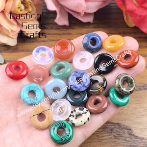 May include: A selection of gemstone donut beads in a variety of colours, including red, blue, green, and yellow. The beads are circular with a hole in the middle. The text "Lasting Gems Crafts" and a website address are visible.