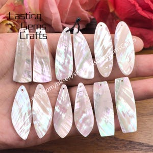 Könnte beinhalten: Eine Sammlung schillernder Perlmutt-Anhänger in verschiedenen Formen, darunter Tropfen- und längliche Designs. Die Anhänger haben einen perlmuttartigen Glanz mit zarten rosa und grünen Farbtönen. Das Bild enthält den Text "Lasting Gems Crafts".