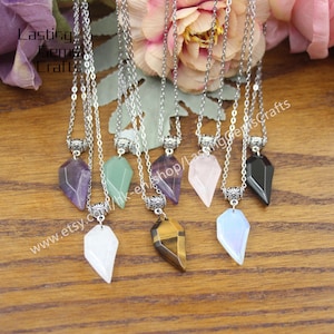 May include: A set of eight silver necklaces with different coloured gemstone pendants. The pendants are shaped like a pointed teardrop and are made of amethyst, green aventurine, rose quartz, tiger's eye, opal, and black onyx.