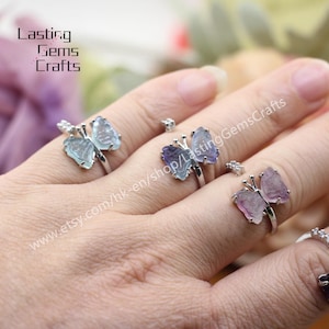 May include: Three silver rings featuring butterfly-shaped settings. The butterflies are crafted from different coloured gemstones: light blue, purple, and pink. The rings are adjustable and can be worn on any finger.