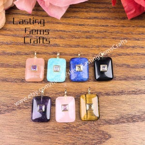May include: Seven rectangular gemstone pendants in various colors, including pink, blue, and black, each with a small square accent stone. The pendants are displayed on a wooden surface. The text "Lasting Gems Crafts" is visible.