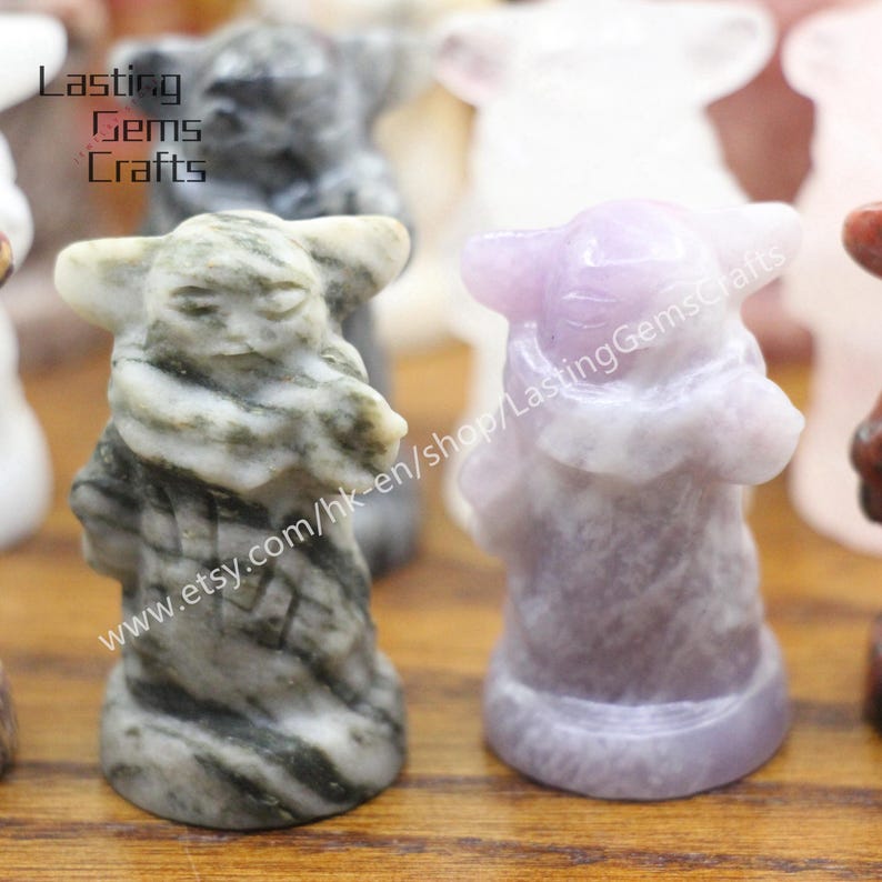 May include: Two small carved figurines of a popular fictional character. The figurine on the left is made of gray and white marble with black streaks. The figurine on the right is made of light purple amethyst. Both figurines are about 4 inches tall.