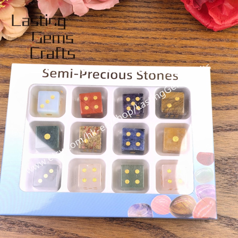 May include: A set of twelve semi-precious stone dice in a white box. Each die has a different color and pattern, with gold-colored dots indicating the numbers. The box is labeled "Semi-Precious Stones."