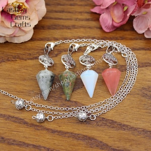 May include: Three silver chain pendulums with tree of life charms and different coloured crystal points. The crystals are green, white, and pink.