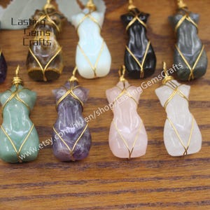 May include: Assortment of eight different colored gemstone pendants, each wrapped in gold wire, in the shape of a female torso. The gemstones are amethyst, rose quartz, green aventurine, tiger's eye, clear quartz, black obsidian, and grey agate.