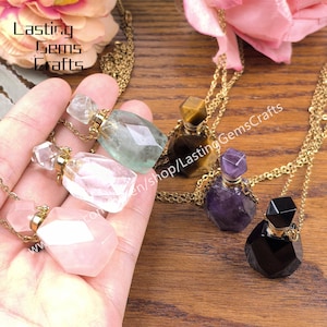 May include: A collection of gemstone perfume bottle pendants on gold chains. The bottles are various colors, including pink, green, purple, and black. The bottles have faceted, geometric shapes and are displayed on a wooden surface.