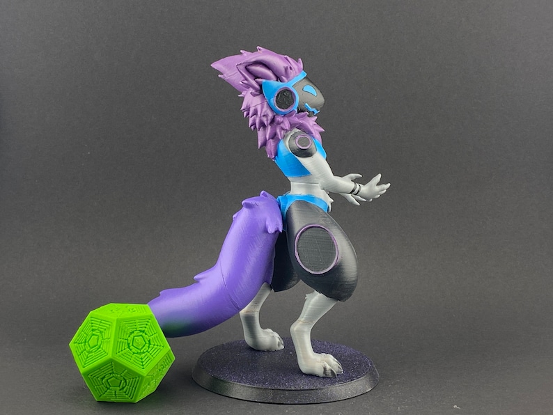 May include: A 3D printed figurine of a purple and white furry creature with a blue and white outfit. The creature has a long purple tail and is standing on a black base. A green geometric object is in the foreground.