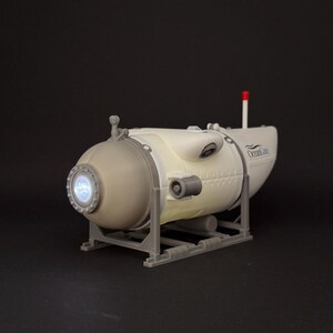 K&ouml;nnte beinhalten: Ein Modell-U-Boot in Wei&szlig; und Grau mit einem beleuchteten kreisf&ouml;rmigen Fenster und dem Text "Ocean Life". Es hat eine rote Antenne und steht auf einem grauen Rahmen. Das Modell ist mit Nieten und anderen Details versehen.
