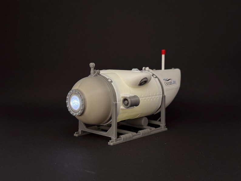 K&ouml;nnte beinhalten: Ein Modell-U-Boot in Wei&szlig; und Grau mit einem beleuchteten kreisf&ouml;rmigen Fenster und dem Text "Ocean Life". Es hat eine rote Antenne und steht auf einem grauen Rahmen. Das Modell ist mit Nieten und anderen Details versehen.