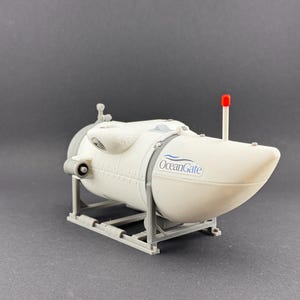 K&ouml;nnte beinhalten: Ein wei&szlig;es U-Boot-Modell mit dem Logo "OceanGate". Es hat eine rote Antenne und steht auf einem grauen St&auml;nder. Das Modell ist ein detaillierter Nachbau eines Tauchboots.