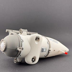 K&ouml;nnte beinhalten: Ein 3D-gedrucktes Modell eines U-Boot-&auml;hnlichen Fahrzeugs. Das Modell ist &uuml;berwiegend cremewei&szlig; mit grauen und silbernen Akzenten. Es hat einen abgerundeten vorderen Bereich, einen stromlinienf&ouml;rmigen K&ouml;rper und eine rote Spitze. Das Design umfasst verschiedene mechanische Details.