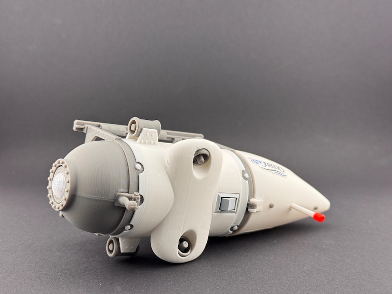 K&ouml;nnte beinhalten: Ein 3D-gedrucktes Modell eines U-Boot-&auml;hnlichen Fahrzeugs. Das Modell ist &uuml;berwiegend cremewei&szlig; mit grauen und silbernen Akzenten. Es hat einen abgerundeten vorderen Bereich, einen stromlinienf&ouml;rmigen K&ouml;rper und eine rote Spitze. Das Design umfasst verschiedene mechanische Details.