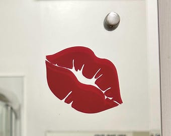 Puede incluir: Una pegatina de labios rojos sobre un fondo blanco. La pegatina es un diseño simple de un par de labios con un contorno blanco.