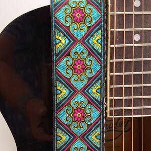 Könnte beinhalten: Ein Gitarrengurt mit einem farbenfrohen geometrischen Muster in Blautönen, Rosa, Gelb und Schwarz. Das Muster zeigt sich in sich wiederholenden Diamantenformen mit floralen Designs.