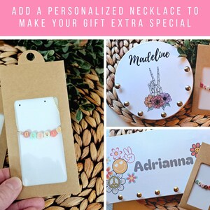 May include: Personalized necklaces with colorful letter beads on thin chains, presented in brown cardboard packaging. The display includes white cards featuring the names Madeline and Adrianna, alongside graphic illustrations of a skeleton hand, flowers, and smiley faces.
