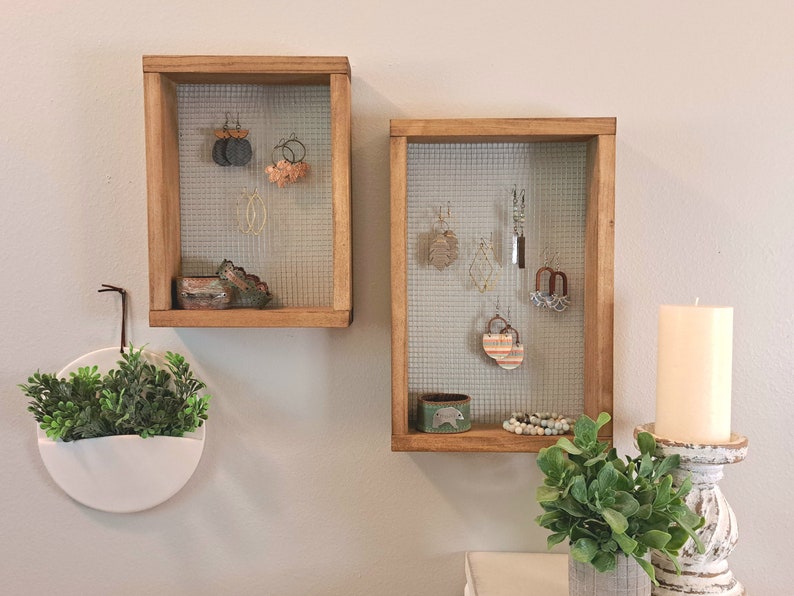 May include: Two rectangular wooden wall-mounted jewellery organisers with wire mesh backing. Each frame displays various hanging earrings and small accessories on the mesh, with additional items resting on the bottom wooden ledge of each frame.