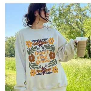 May include: A beige sweatshirt with a floral design and the text "tune thy heart to sing thy grace".