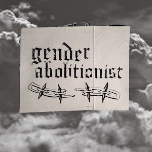 May include: A beige fabric patch with black text that reads "gender abolitionist" and two black barbed wire chains, one broken, against a cloudy background.