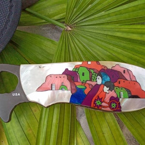 May include: A knife with a colorful, abstract design on the handle. The design features a multi-colored cityscape with red, purple, green, and blue accents. The knife handle is made of mother-of-pearl and has the word "USA" inscribed on it.