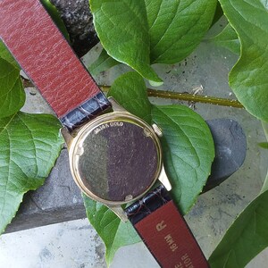 May include: A gold-tone wristwatch with a brown leather band. The back of the watch case is visible and says "14K Gold".