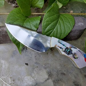 May include: A silver pocket knife with a mother of pearl handle featuring a colorful design of a person holding balloons. The blade is marked "Bocker" and has a slight curve.