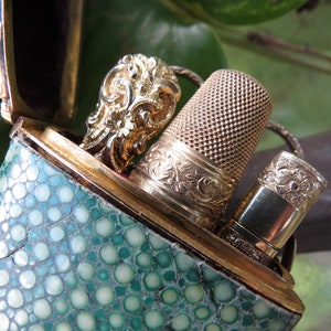 May include: A green leather case with a gold metal clasp and a gold metal thimble and a gold metal needle threader inside.