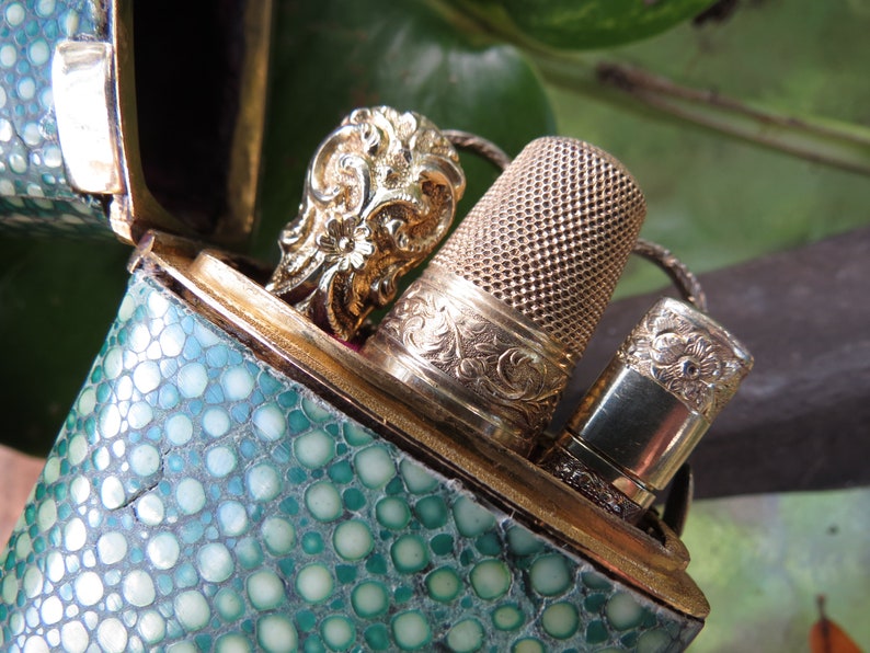May include: A green leather case with a gold metal clasp and a gold metal thimble and a gold metal needle threader inside.