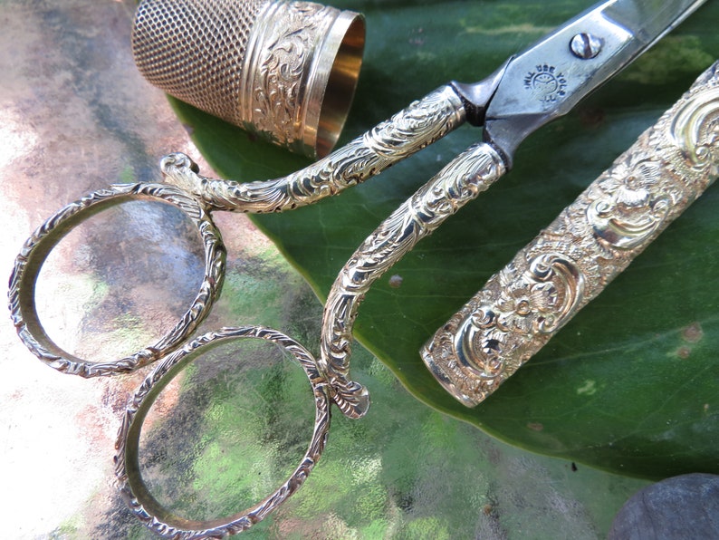 May include: A set of antique gold-toned scissors with a decorative floral design. The scissors are in a case with a matching design. The case is open and the scissors are partially extended.
