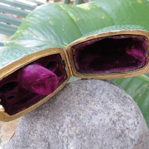 May include: A green and gold hinged box with a velvet interior. The box is open and the velvet lining is visible.