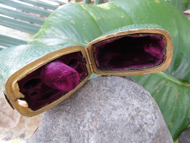 May include: A green and gold hinged box with a velvet interior. The box is open and the velvet lining is visible.