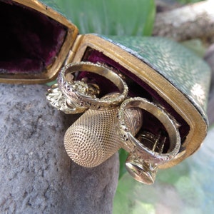 May include: A green leather case with gold trim and a velvet lining, containing three gold thimbles and a gold ring.